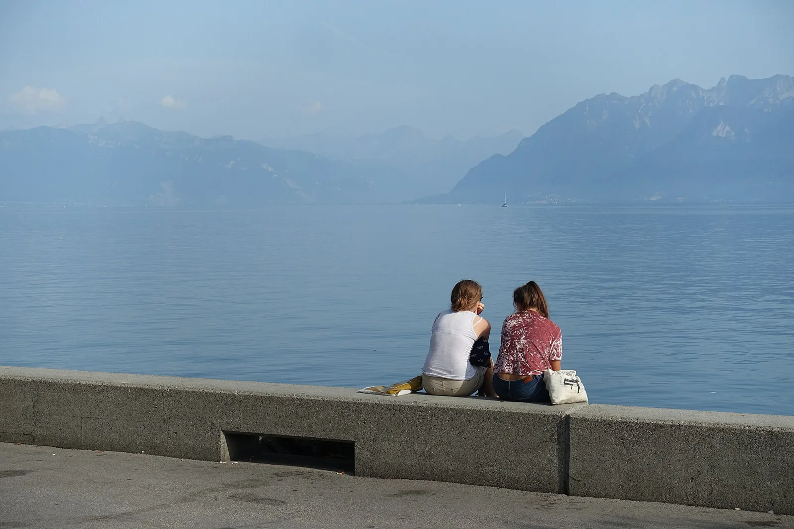 Deux personnes assises sur le quai à Ouchy, face au lac Léman et aux Alpes