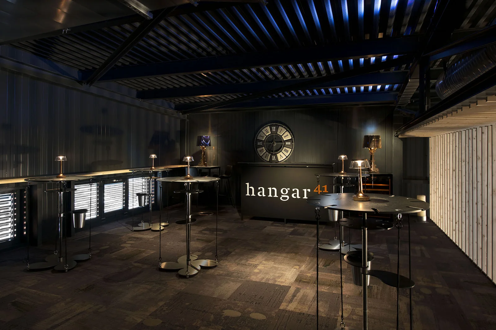 Mezzanine du Hangar41 à Sion avec tables hautes et lampes