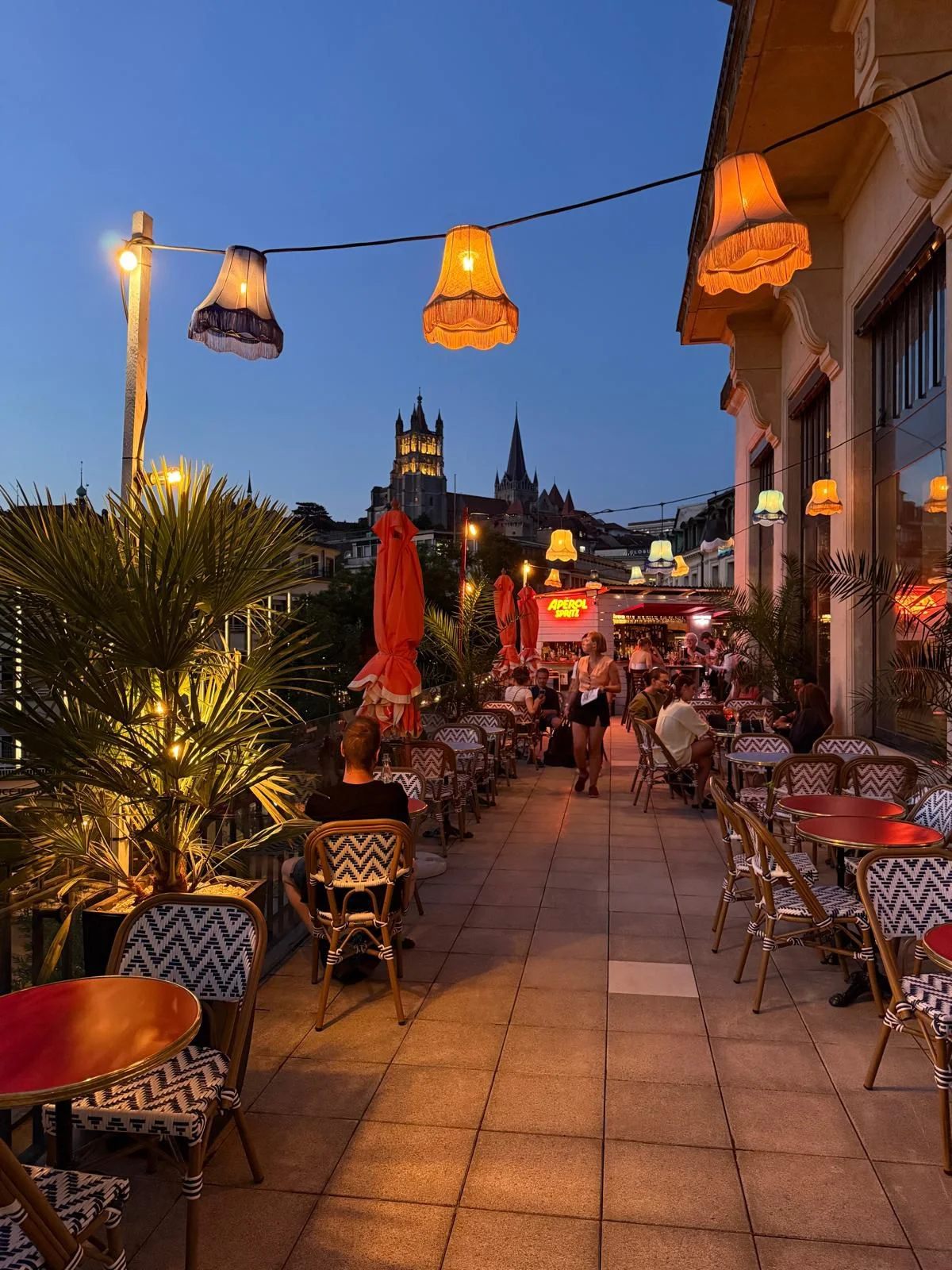 Terrasse du Lausanne Cocktail Club en soirée, lampes vintage et cathédrale