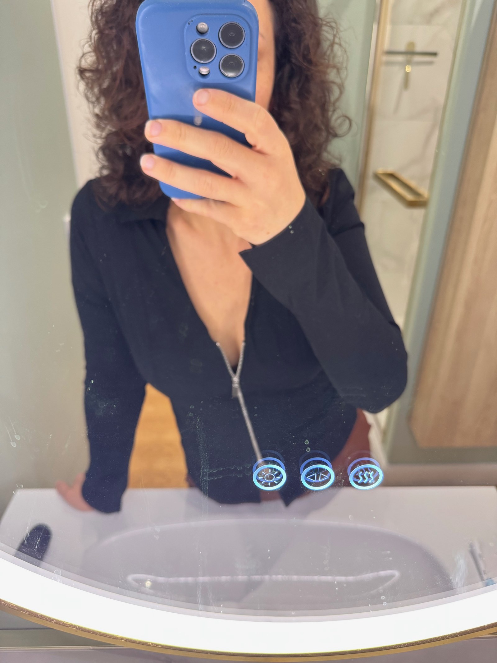 Léna fait un selfie dans le miroir en chemisier noir à fermeture éclair, le Natel devant le visage