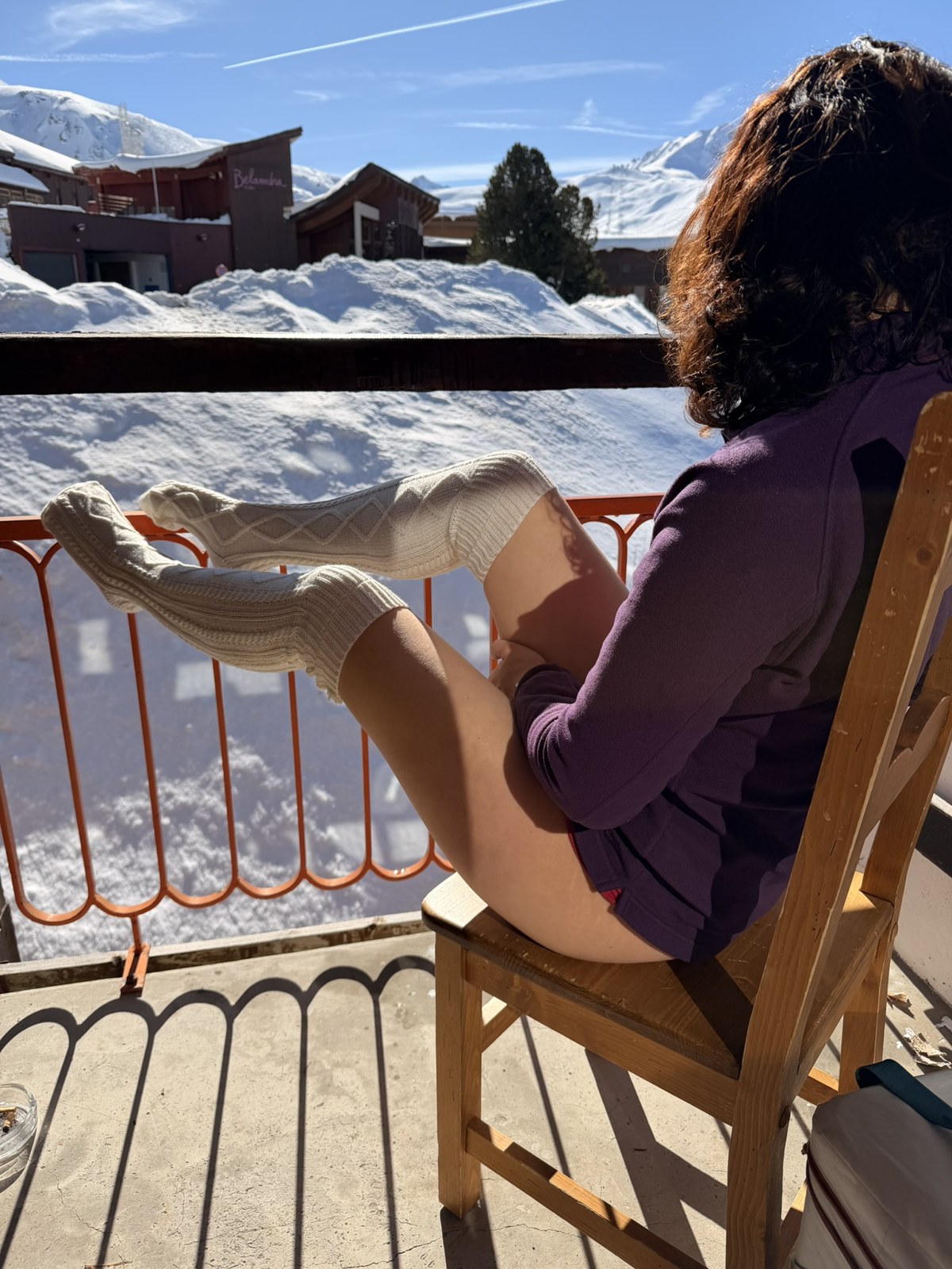 Léna assise sur une terrasse de chalet enneigée, vue sur les montagnes, en pull et collants